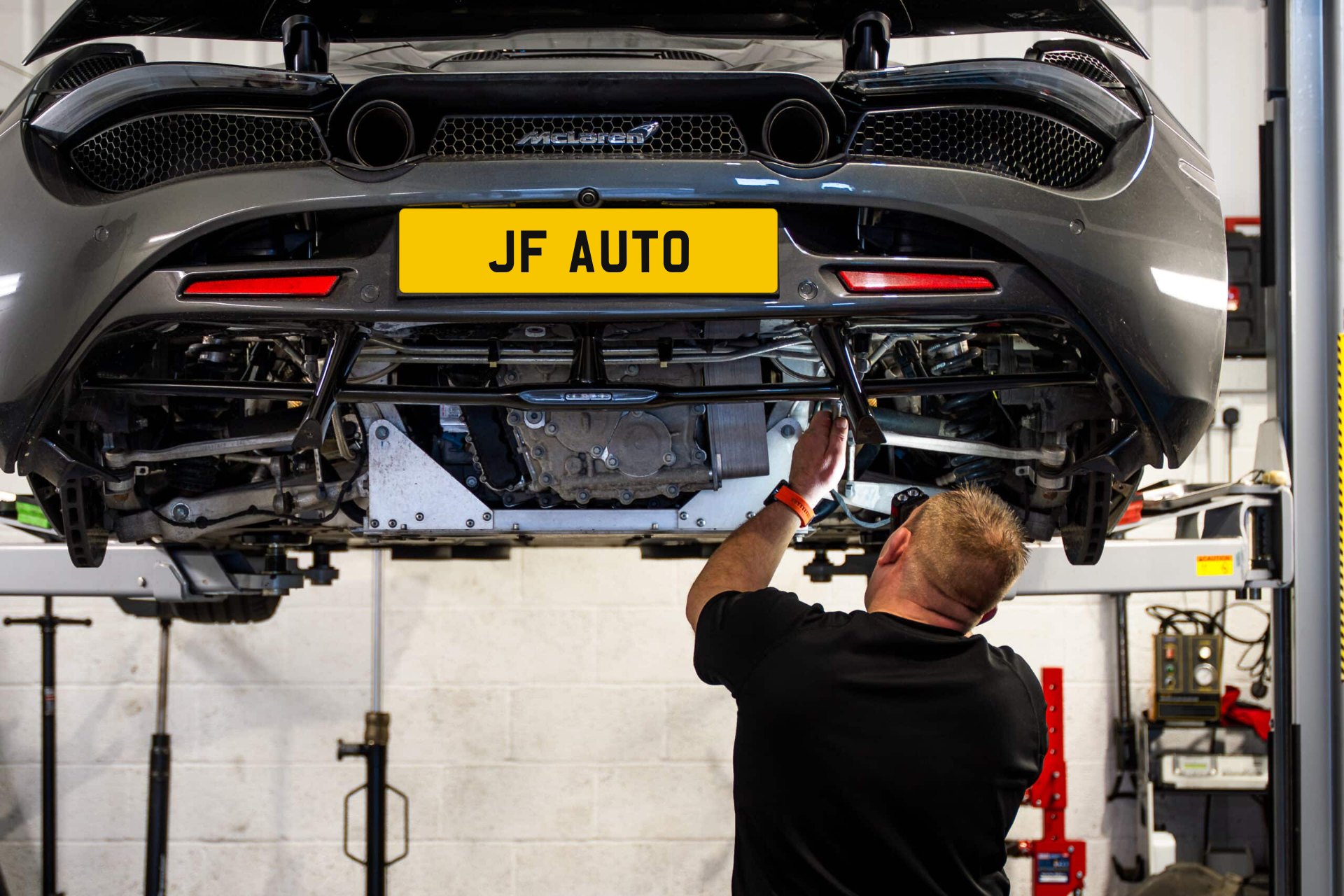Technician working under a McLaren on the ramp at JF Automotive in Maidstone